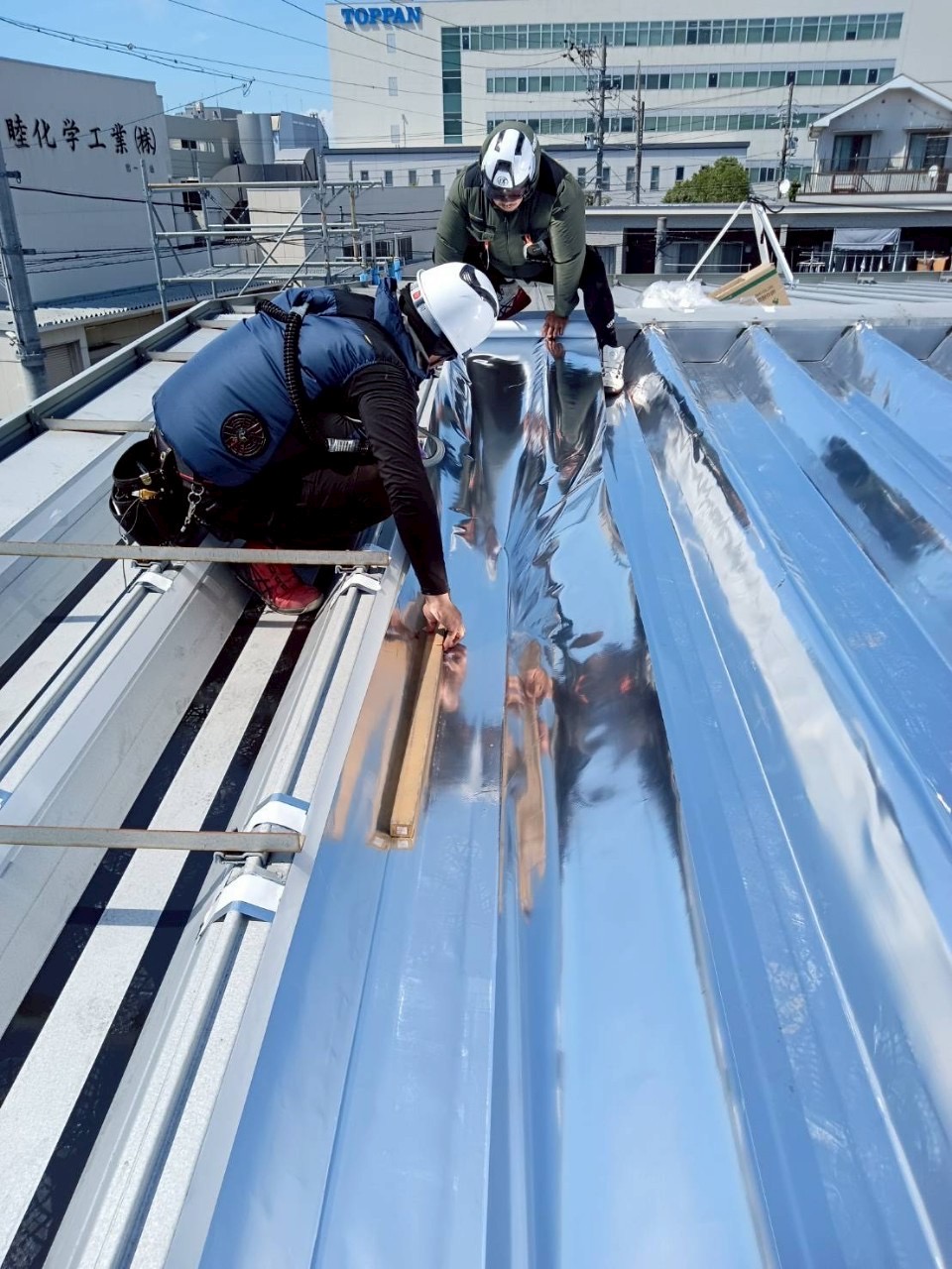 安全帯を着用して屋根上で連携する施工スタッフ